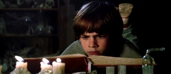 Menino lendo um livro à luz de velas num sótão