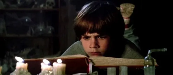 Menino lendo um livro à luz de velas num sótão
